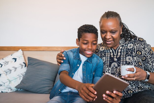 Portret van grootmoeder en kleinkind selfie met digitale tablet zittend op de banklaag thuis. Familie en levensstijlconcept.