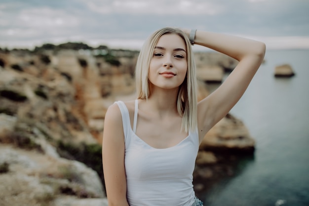 Portret van het aantrekkelijke blonde vrouw stellen op rotsachtig strand met schoonheidslandschap.