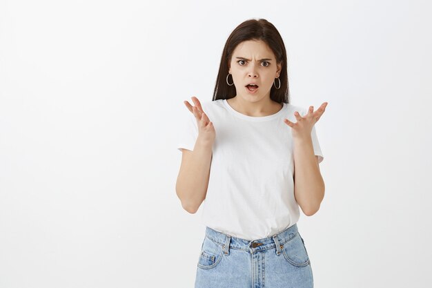 Portret van het boze teleurgestelde jonge vrouw stellen tegen witte muur