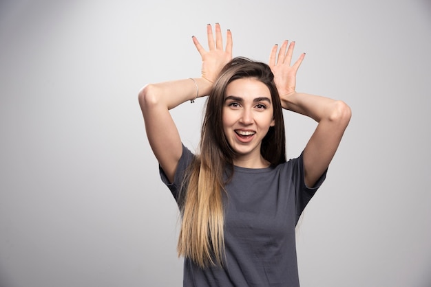 Portret van het gelukkige vrouw stellen en konijntjesoren over grijze achtergrond zetten.