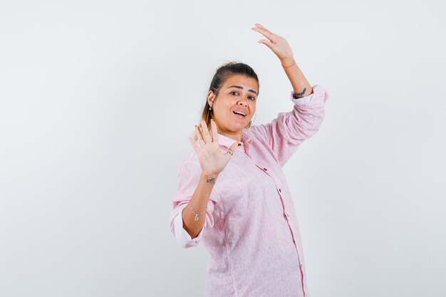 Portret van het jonge vrouwelijke stellen met opgeheven handen in roze overhemd en op zoek charmant vooraanzicht