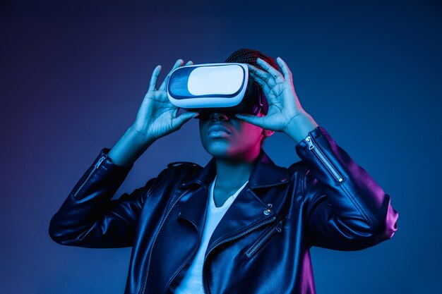 Portret van het spelen van een jonge vrouw in VR-bril in neonlicht op blauw