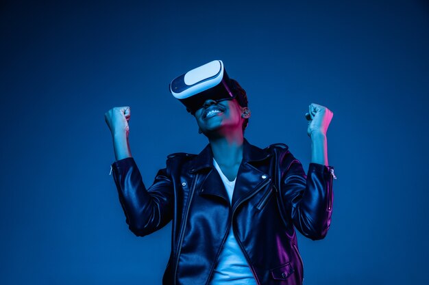 Portret van het spelen van een jonge vrouw in VR-bril in neonlicht op blauw