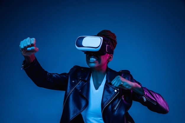 Portret van het spelen van een jonge vrouw in VR-bril in neonlicht op blauw