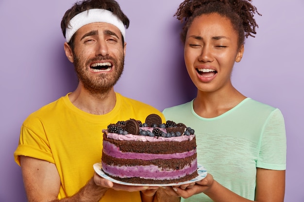 Portret van het treurige actieve paar poseren met een grote taart close-up