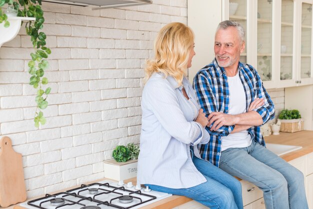 Portret van hogere paarzitting op keukenteller die elkaar bekijken