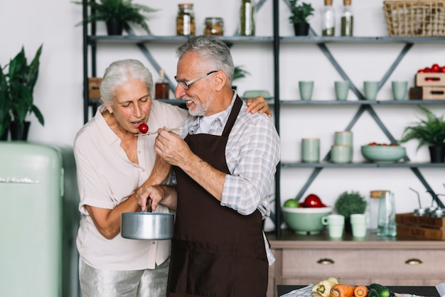 Gratis foto portret van hogere vrouw die voedsel eet dat door zijn echtgenoot in de keuken wordt voorbereid