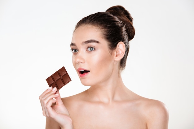 Portret van hongerige halfnaakte vrouw die met donker haar chocoladereep eet die niet op een dieet is