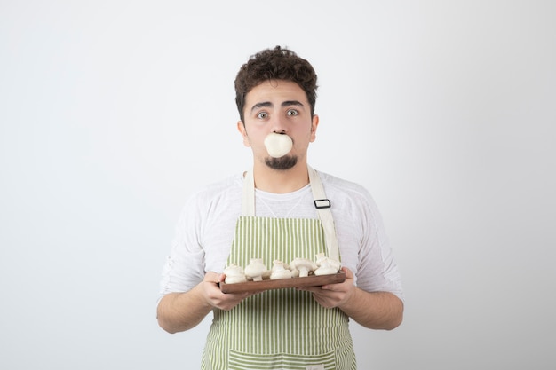 Portret van hongerige mannelijke kok die rauwe champignons op wit houdt