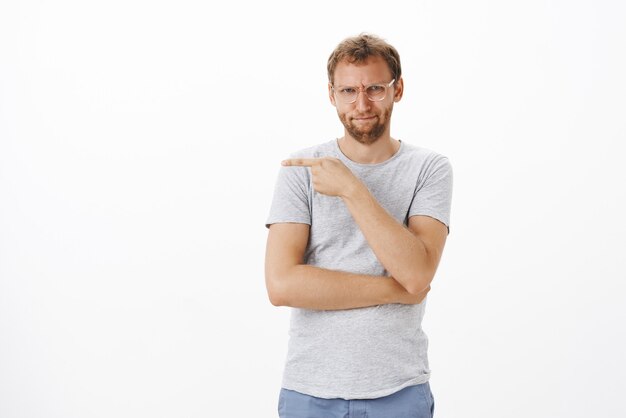 Portret van intens gestoorde en geïrriteerde knappe volwassen man met borstelharen in glazen fronsend tuitende lippen krijgen man naar links wijzend naar collega die hij haat over witte muur