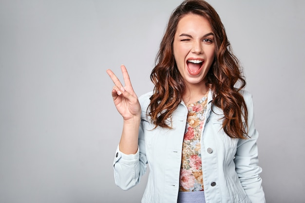 Portret van jong modieus het lachen model in kleurrijke toevallige de zomerkleren met natuurlijke make-up op grijs