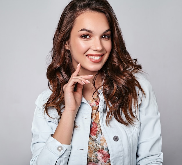 Portret van jong modieus het lachen model in kleurrijke toevallige de zomerkleren met natuurlijke make-up op grijs