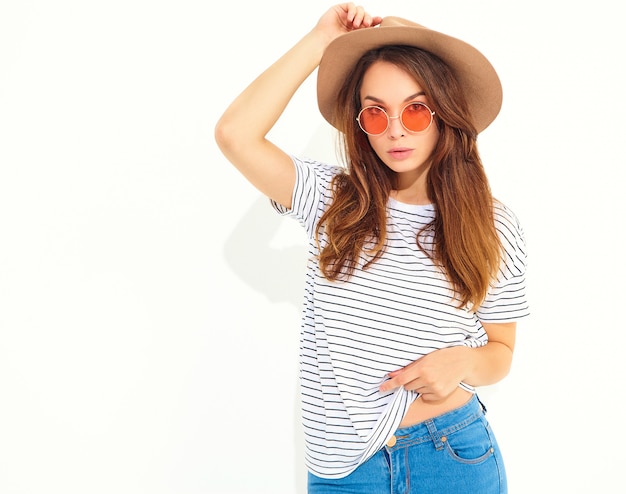 Portret van jong modieus lachend vrouwenmodel in toevallige de zomerkleren in bruine hoed met natuurlijke die make-up op witte muur wordt geïsoleerd.