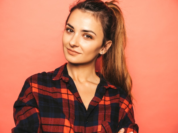 Portret van jong mooi glimlachend hipster meisje in trendy de zomer geruit overhemd en jeanskleren. Het sexy onbezorgde vrouw stellen dichtbij roze muur in studio. Positief model zonder make-up