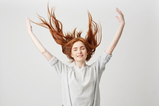 Portret van jong vrolijk mooi roodharigemeisje die met gesloten ogen glimlachen die haar schudden.