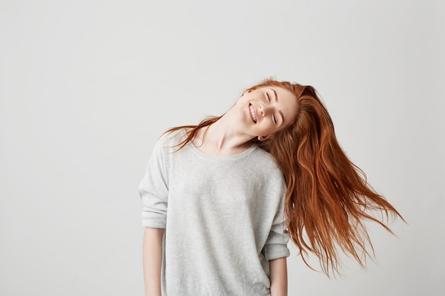 Portret van jong vrolijk mooi roodharigemeisje die met gesloten ogen glimlachen die hoofd en haar schudden.