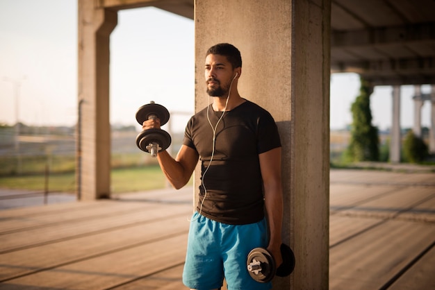 Gratis foto portret van jonge aantrekkelijke sportman die gewichten opheft en bicepsoefening doet