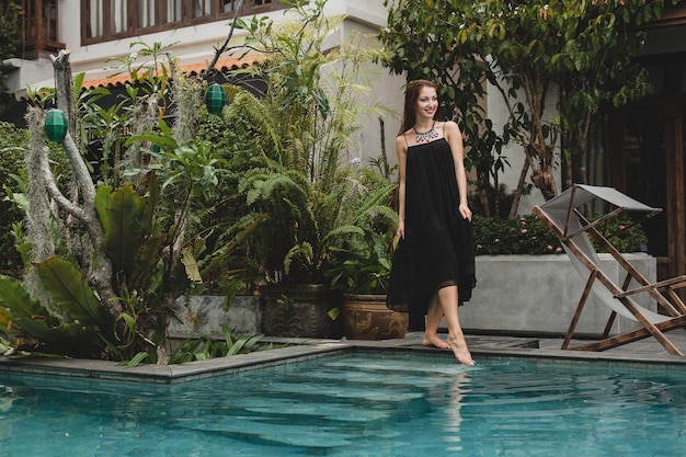Portret van jonge aantrekkelijke vrouw in elegante jurk, strooien hoed, zomerstijl, modetrend, vakantie, glimlachen, stijlvolle accessoires, zonnebril, poseren op tropische villa op Bali