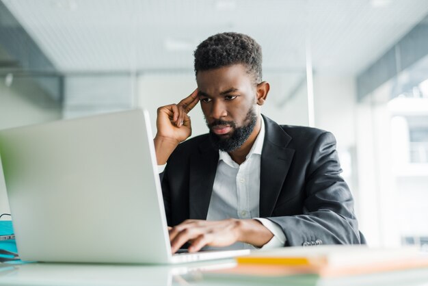 Portret van jonge Afrikaanse man te typen op de laptop in het kantoor