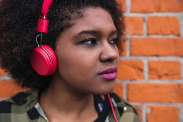 Portret van jonge Afro-Amerikaanse Latijns-vrouw, luisteren naar muziek met een koptelefoon in de straat. Buitenshuis.