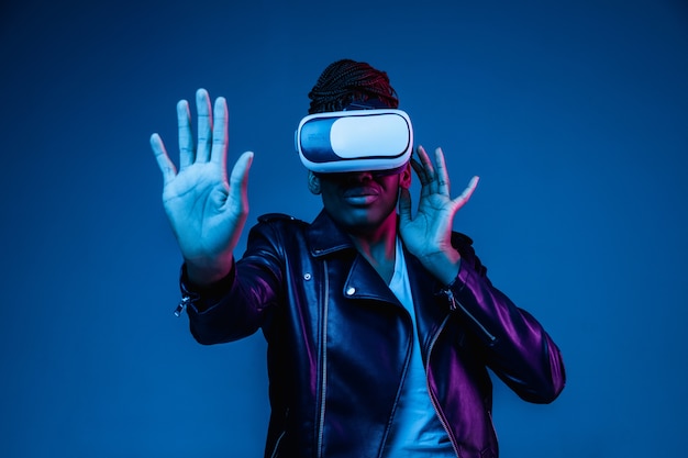 Portret van jonge Afro-Amerikaanse vrouw spelen in VR-bril in neonlicht op blauw.