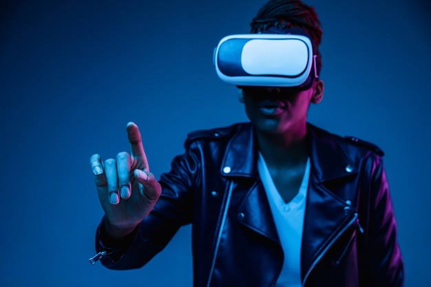 Portret van jonge Afro-Amerikaanse vrouw spelen in VR-bril in neonlicht op blauw.