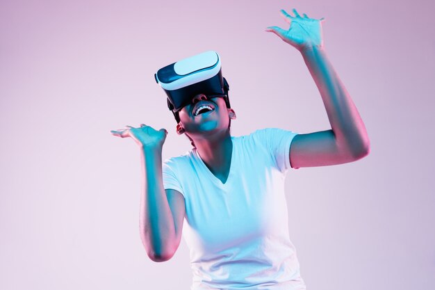 Portret van jonge Afro-Amerikaanse vrouw spelen in VR-bril in neonlicht op verloop