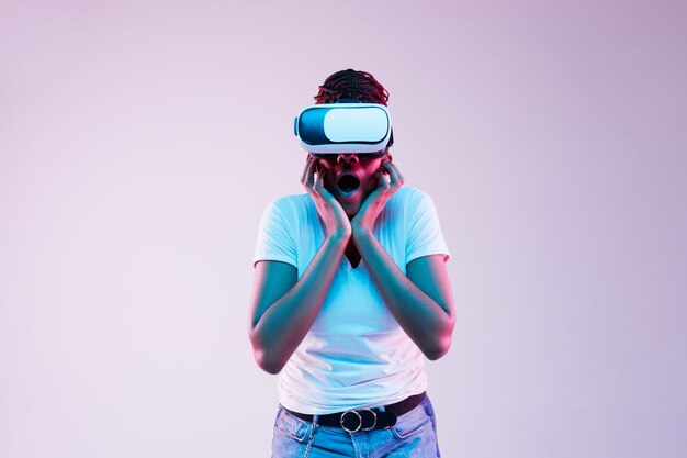 Portret van jonge Afro-Amerikaanse vrouw spelen in VR-bril in neonlicht op verloop