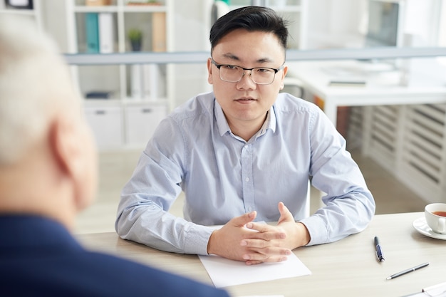 Portret van jonge aziatische man beantwoorden van vragen tijdens sollicitatiegesprek zitten tegenover senior manager, kopie ruimte