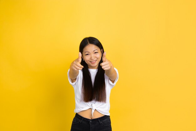 Portret van jonge Aziatische vrouw dat op gele muur wordt geïsoleerd