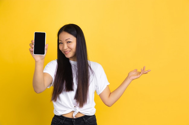 Portret van jonge Aziatische vrouw dat op gele muur wordt geïsoleerd