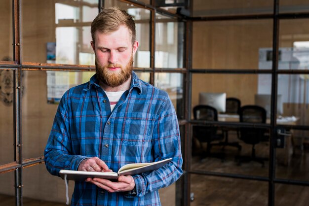 Portret van jonge bebaarde man lezen dagboek in office