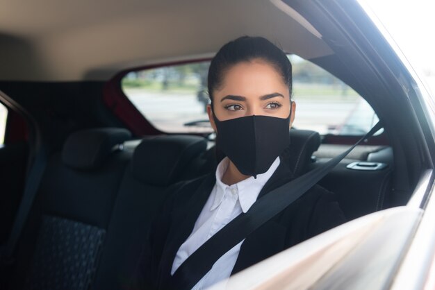 Portret van jonge bedrijfsvrouw die gezichtsmasker dragen op haar weg naar het werk in een taxi