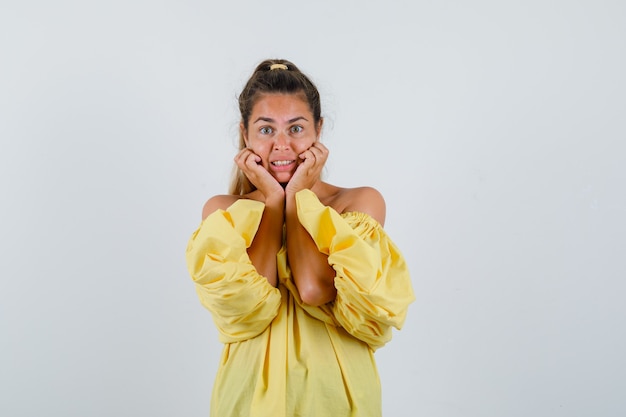 Portret van jonge dame kussen gezicht op haar handen in gele jurk en op zoek verontrust vooraanzicht