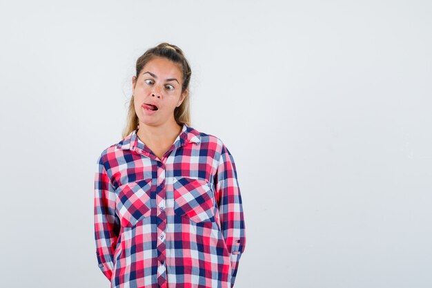 Portret van jonge dame tong uitsteekt, ogen loensen in geruit overhemd en op zoek grappig vooraanzicht