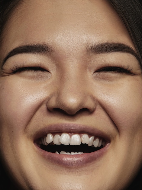 Portret van jonge en emotionele chinese vrouw close-up. Zeer gedetailleerde fotoshoot van een vrouwelijk model met een goed onderhouden huid en een heldere gezichtsuitdrukking. Concept van menselijke emoties. Glimlachen naar de camera.