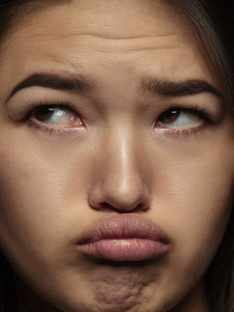 Portret van jonge en emotionele chinese vrouw close-up. Zeer gedetailleerde fotoshoot van een vrouwelijk model met een goed onderhouden huid en een heldere gezichtsuitdrukking. Concept van menselijke emoties. Ziet er verdrietig en beledigd uit.