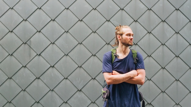 Gratis foto portret van jonge mannelijke reiziger met gekruist wapen status dichtbij geweven muur