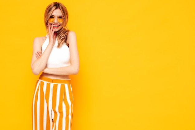 Portret van jonge mooie lachende blonde vrouw in trendy zomerkleren zorgeloze vrouw poseren in de buurt van gele muur in studio Positief model plezier binnenshuis vrolijk en gelukkig
