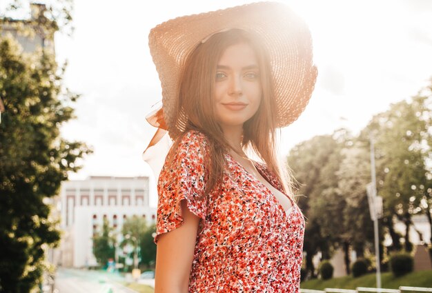 Portret van jonge mooie lachende hipster meisje in trendy zomer zonnejurk. Sexy zorgeloos vrouw die zich voordeed op de straat achtergrond in hoed bij zonsondergang. Positief model buitenshuis