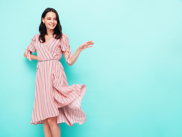 Portret van jonge mooie lachende vrouw in trendy roze zomerjurk Sexy zorgeloze vrouw poseren in de buurt van blauwe muur in studio Positief model plezier binnenshuis vrolijk en gelukkig