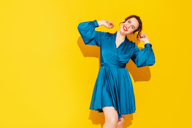 Portret van jonge mooie lachende vrouw in trendy zomer blauwe jurk sexy zorgeloze vrouw poseren in de buurt van gele muur in studio positief model plezier en gek vrolijk en gelukkig