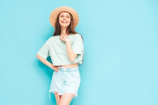 Portret van jonge mooie lachende vrouw in trendy zomer jeans rok zorgeloze vrouw poseren in de buurt van blauwe muur in studio Positief model plezier binnenshuis vrolijk en gelukkig In hoed