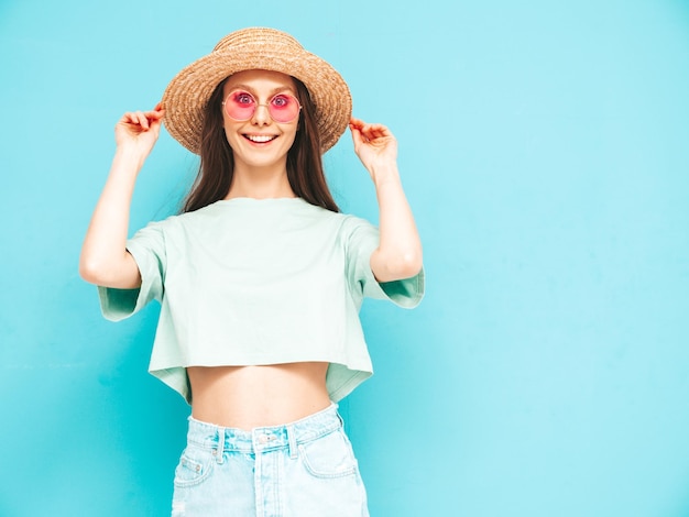 Portret van jonge mooie lachende vrouw in trendy zomer jeans rok zorgeloze vrouw poseren in de buurt van blauwe muur in studio Positief model plezier binnenshuis vrolijk en gelukkig In hoed