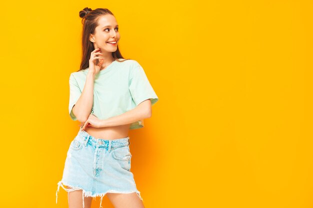 Portret van jonge mooie lachende vrouw in trendy zomer jeans rok zorgeloze vrouw poseren in de buurt van gele muur in studio positief model plezier binnenshuis vrolijk en gelukkig