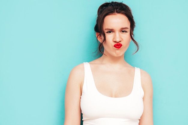 Portret van jonge mooie lachende vrouw in trendy zomerkleren Sexy zorgeloze vrouw poseren in de buurt van blauwe muur in studio Positief model met plezier en gek maakt eend gezicht rode lippen