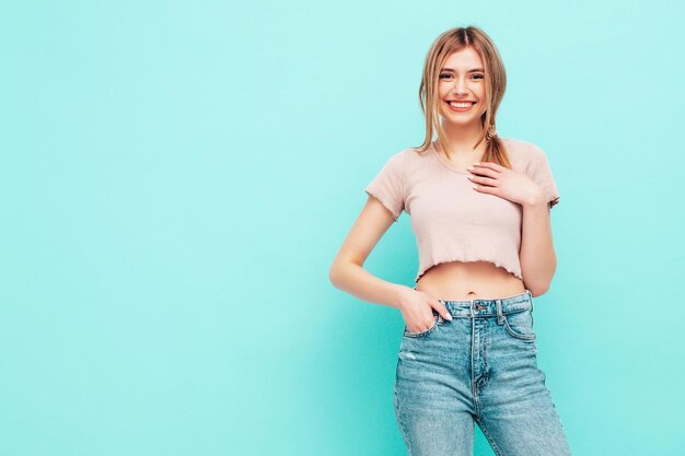 Portret van jonge mooie lachende vrouw in trendy zomerkleren Sexy zorgeloze vrouw poseren in de buurt van blauwe muur in studio Positieve blond model plezier en gek vrolijk en gelukkig