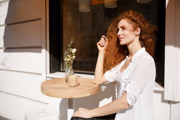 Portret van jonge mooie roodharige vrouw zitten in een café