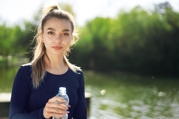 Portret van jonge mooie vrouw die blauw sportkleding drinkwater draagt bij park