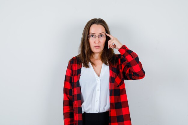 Portret van jonge mooie vrouw met vinger op tempels in casual outfit en peinzend vooraanzicht